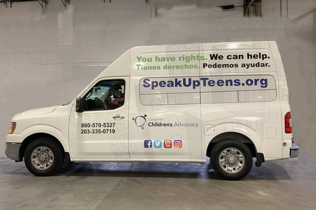 A side profile of the Center for Children's Advocacy's Mobile Legal Office. The MLO is a white van with CCA's information on the side. The text on the van, in English and Spanish, reads "You have rights. We can help. SpeakUpTeens.org".